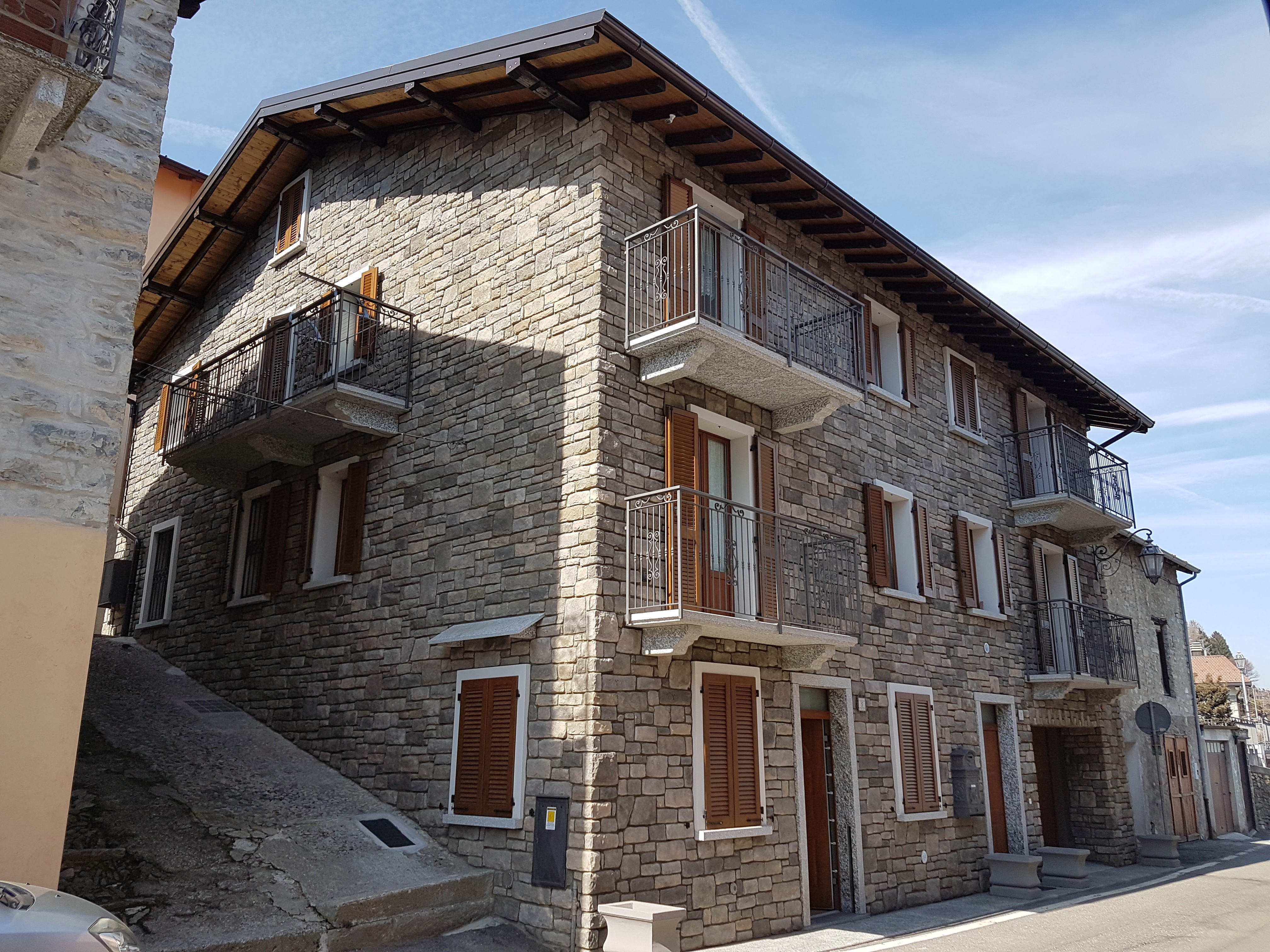 Edificio residenziale con rivestimento in pietra naturale, balconi in ferro battuto e persiane in legnoEdificio residenziale con rivestimento in pietra naturale, balconi in ferro battuto e persiane in legno
